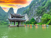 A traditional curved-roof pavilion sits on a green lake beside limestone cliffs.