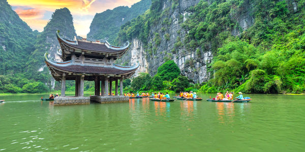 A traditional curved-roof pavilion sits on a green lake beside limestone cliffs.