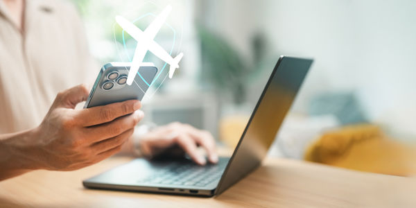Traveler using a smartphone and laptop with airplane protection icon, representing travel insurance, trip coverage, claim management, travel planning, financial security, and safe journeys.
