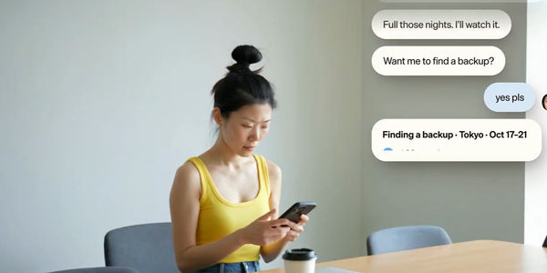 A woman in a yellow top sits at a table reading her phone