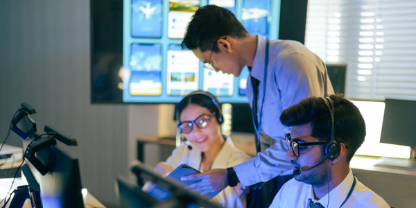 Three analysts wearing headsets work collaboratively at desks in a control room.