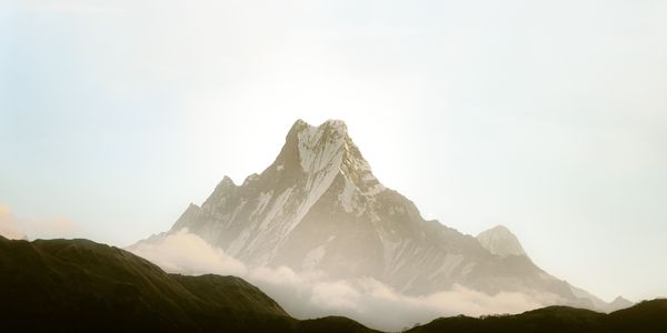 A snow-capped peak rises above dark hills at dawn.