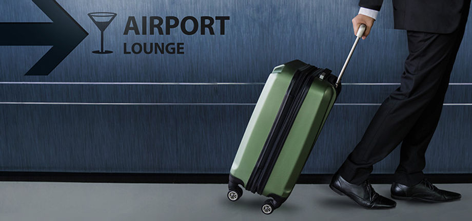 A green suitcase is rolled by a person in an airport lounge.