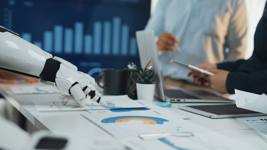 A white robotic hand points over a desk with charts during a business meeting.