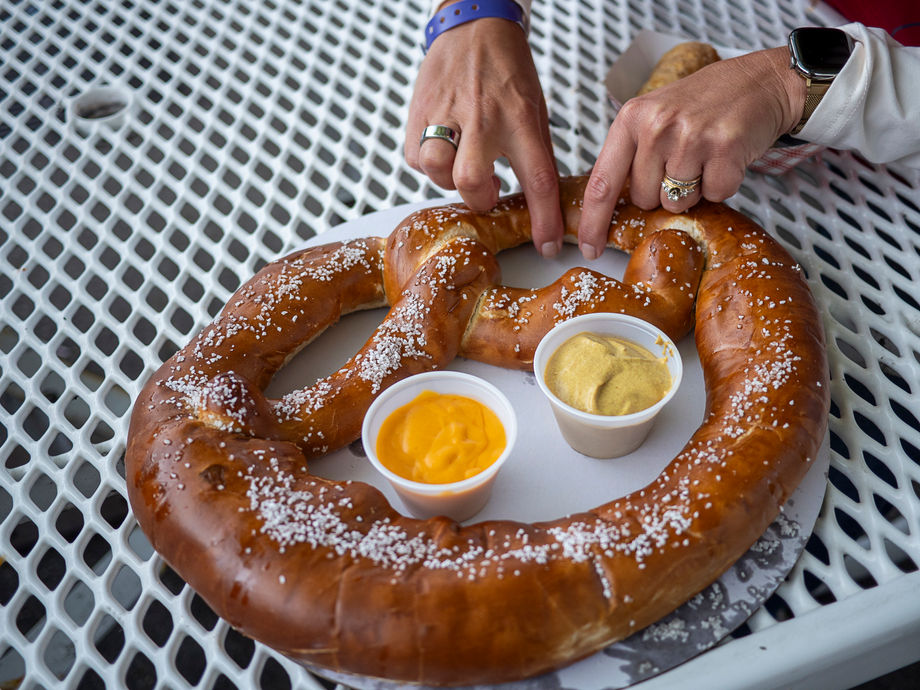 A giant glossy brown pretzel sits on a plate with coarse salt and two dipping sauces.