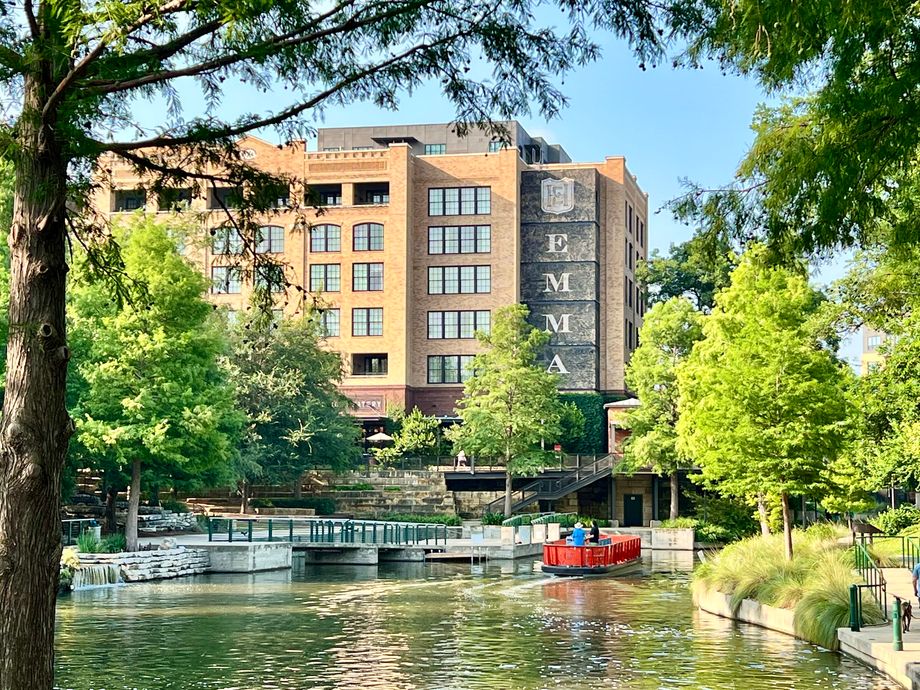 Brick building sits beside a calm canal with a red boat nearby.