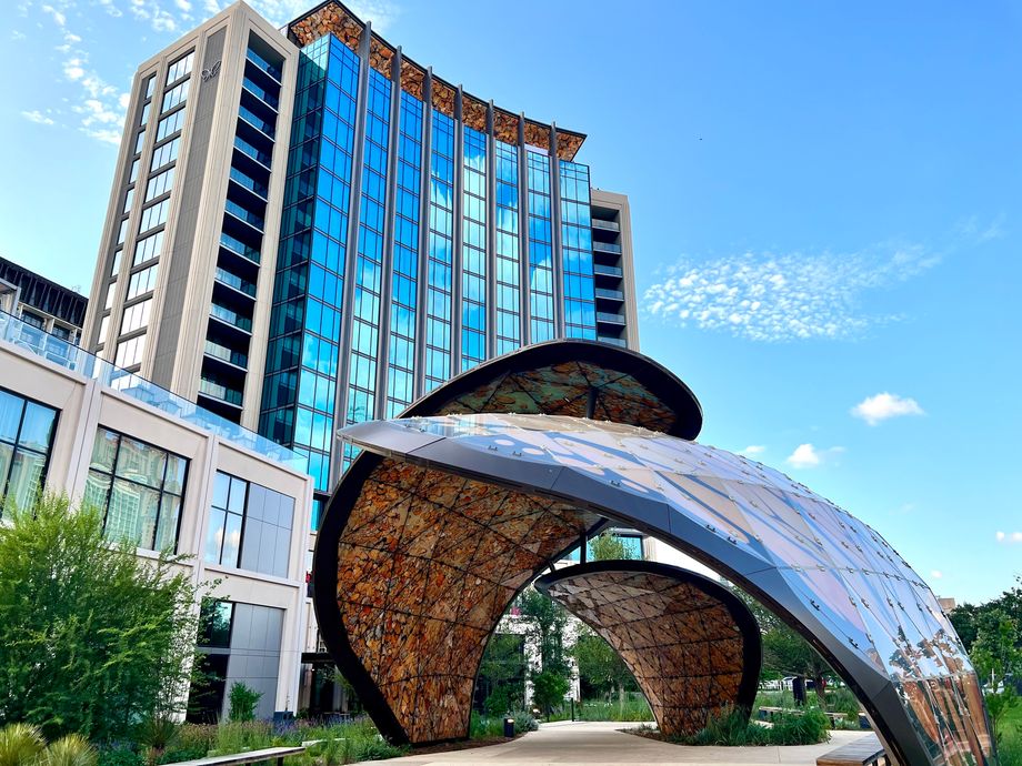 Curved metallic arch sculpture dominates the foreground beside a modern glass building.