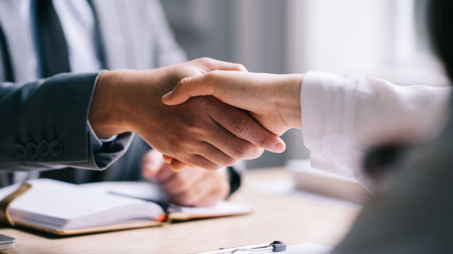 Two people shake hands across a desk