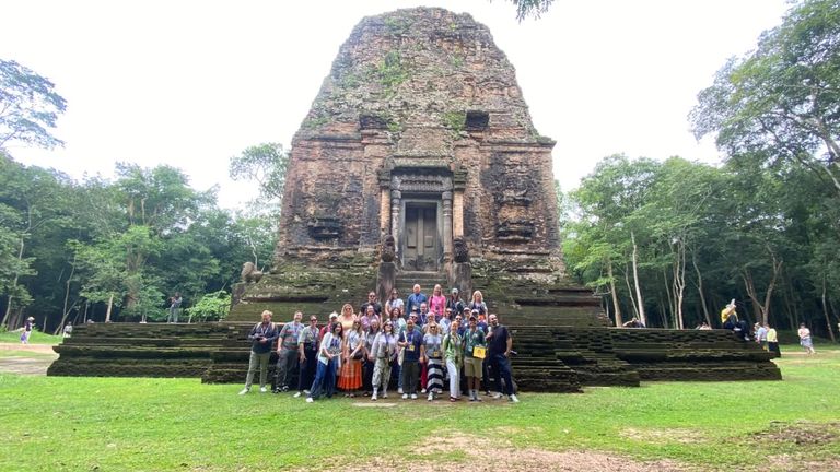 A historic stone temple ruin with a group of visitors at its front steps.