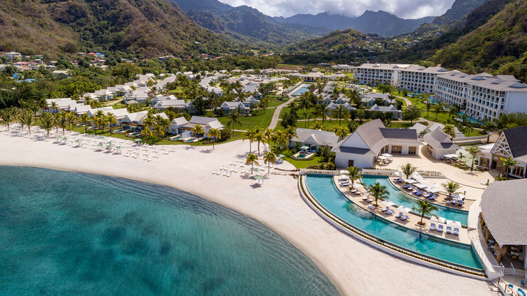 A tropical beach resort with turquoise water and palm trees along a curved shoreline.