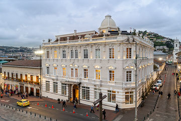 A grand white neoclassical building with a dome stands beside a busy street.