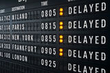 A large airport departure board shows delayed flights with yellow indicators.