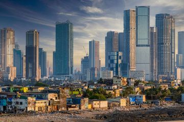 A modern city skyline with tall glass skyscrapers rising above a cluster of low-rise buildings.