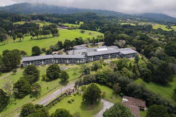 Aerial view of Montara Hotel surrounded by lush green grounds and forested mountains beneath low-hanging clouds.