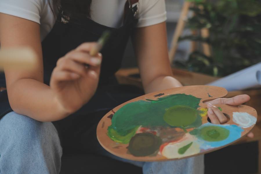 Cropped image of female artist standing in front of an easel and dipping brush into color palette