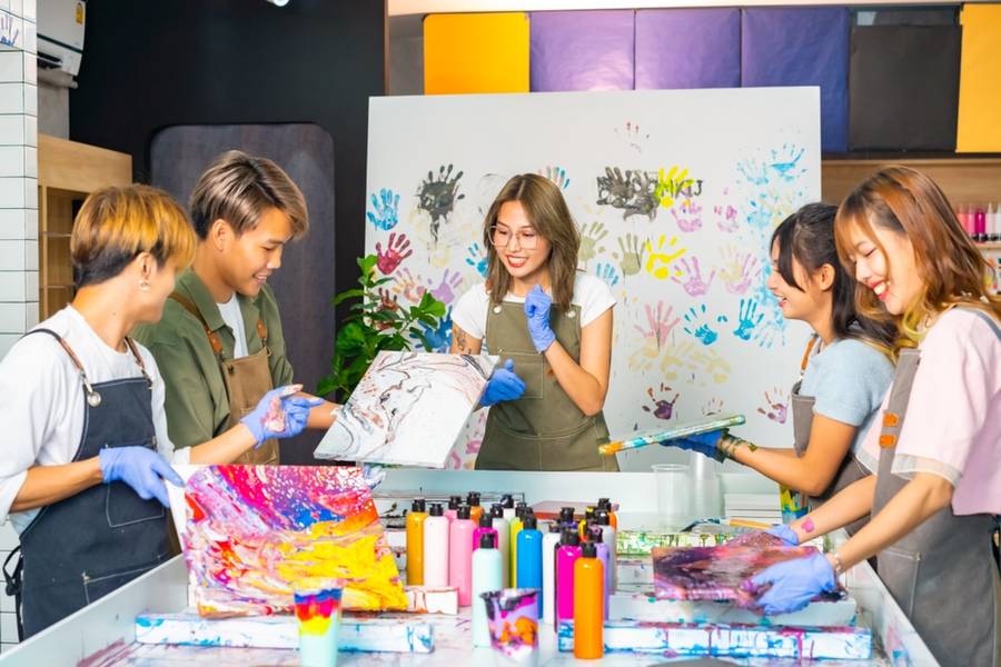 Group of Asian generation z people learning acrylic pouring art on canvas workshop at art studio.