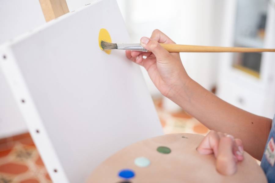 Close-up of boy's hands painting with brush on canvas holding palette. Concept of art and and hobbies.