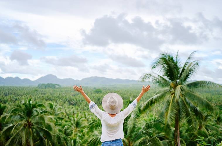 Tropical vacation. Young woman in hat enjoying the view of beautiful coconut palms plantation.