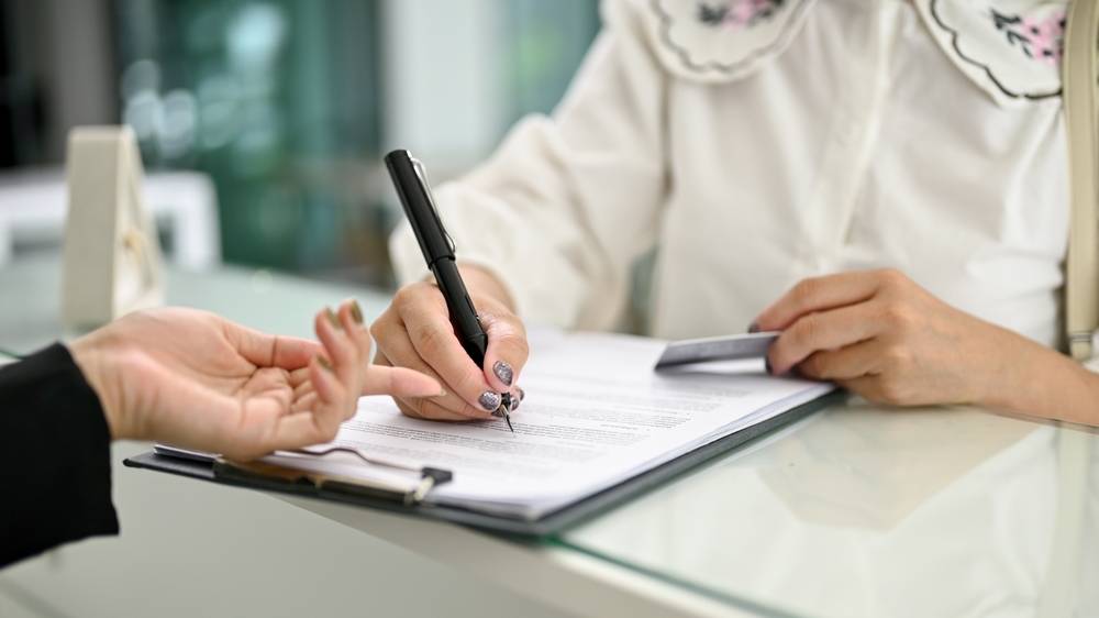 Close-up image of a customer filling out a form and signing her signature on a document at the hotel lobby.