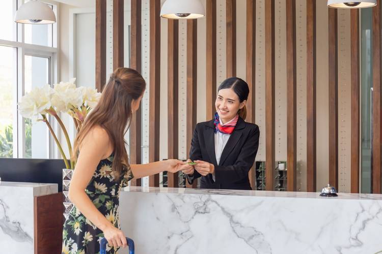 Young Asian woman receptionist at the hotel counter talking with blurred female travelers check-in at the hotel, Female receptionist working in the hotel