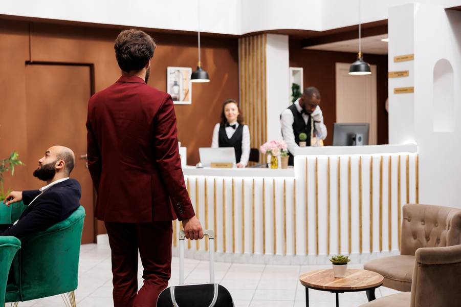 Formal guest enter reception area, carrying suitcase at front desk to do check in process