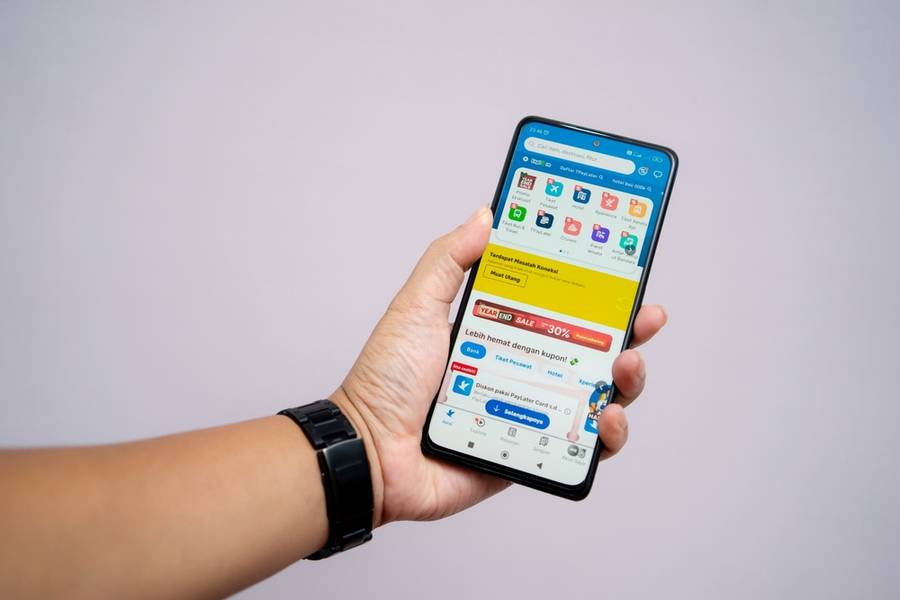 Left hand holding a cellphone displaying the Traveloka application with a white background
