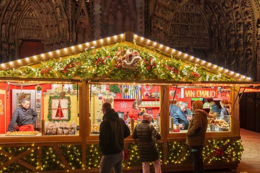  A brightly decorated Christmas market stall offering festive treats and mulled wine, with customers enjoying the holiday ambiance.

