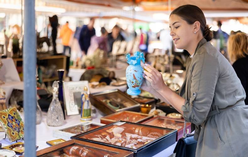 Happy young woman buying retro and antique handicrafts on flea market