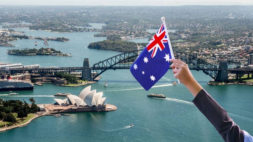 Someone waving an Australian Flag with Sydney Harbour, the Sydney Harbour Bridge and Sydney Opera House in the background.