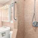 This well-designed bathroom features a fully tiled walk-in shower with a handheld showerhead, built-in grab bars, and modern lighting. The compact yet efficient vanity offers ample storage, making it both stylish and functional in this North Central Phoenix home.