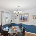 A large window and stylish chandelier highlight this inviting dining space, featuring custom trim details and warm, neutral tones. Ideal for everyday meals or special occasions.