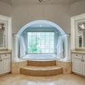 A spa-like experience awaits in this elegant bathroom featuring a soaking tub framed by columns and a glass block window. Relaxation and luxury meet in the heart of Scottsdale.