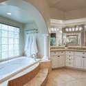 This refined bathroom includes two expansive vanities, a walk-in shower, and stunning tilework under a tray ceiling all wrapped in a soft, spa-inspired color palette.