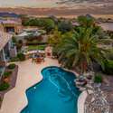 Overlook a breathtaking backyard with a lagoon-style pool, built-in BBQ, and lush palm trees all set beneath colorful skies and scenic mountain silhouettes.