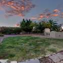 Surrounded by mature landscaping and evening skies, this backyard is a peaceful haven featuring a built-in grill and entertaining-ready green space.