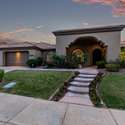 Follow the flower-lined walkway to an elegant arched entrance framed by tropical plants and desert-friendly landscaping. A picture-perfect front yard ready to welcome guests in style.