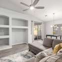 A modern great room layout blends functionality and style with custom built-in shelving, a ceiling fan, and direct access to the backyard. Natural light and tall ceilings enhance the open feel of this central gathering space.