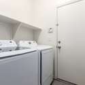 This functional laundry room includes Samsung top-load washer and dryer units, built-in shelving for efficient storage, and direct access to the garage. Clean finishes and neutral tones make laundry tasks effortless in this thoughtfully designed utility space.