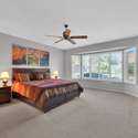 Unwind in this elegant primary bedroom featuring a king-sized bed, bay windows, ceiling fan, and soothing tones. A peaceful setting for a restful night during your Surprise stay.