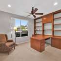 Enjoy productivity and comfort in this sunny home office featuring built-in shelving, a spacious wraparound desk, and a large window with serene backyard views perfect for remote work or reading in this Surprise AZ rental.