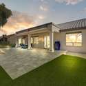 This spacious backyard features an extended travertine patio with artificial turf accents, perfect for outdoor entertaining. Evening lighting enhances the luxurious yet low-maintenance design.