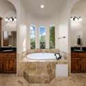 This spa-inspired primary bath offers a deep soaking tub framed by vertical windows and flanked by dual vanities with rich wood cabinetry. A peaceful escape in this beautifully appointed Scottsdale home.
