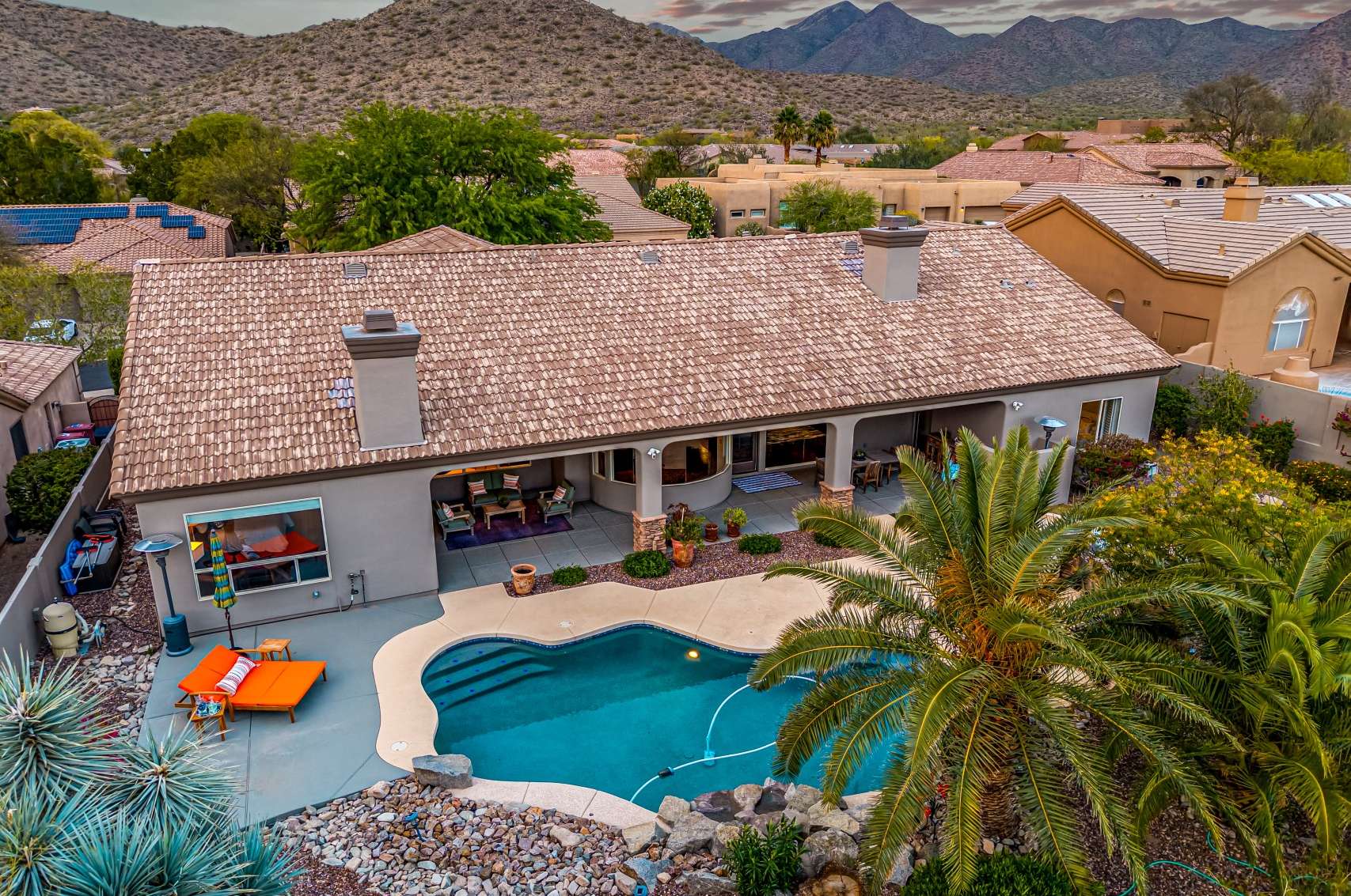 28 of 65. A serene backyard retreat with a shimmering pool, covered lounging space, and vibrant plantings Scottsdale outdoor living at its best.