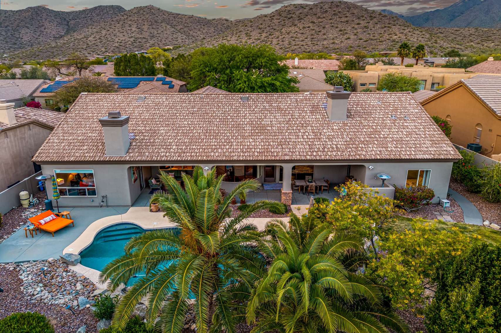64 of 65. This aerial shot captures the full scale of the resort-style backyard, featuring a sparkling pool, covered patio, mature palms, and mountain views. A true desert retreat perfect for entertaining or quiet relaxation.