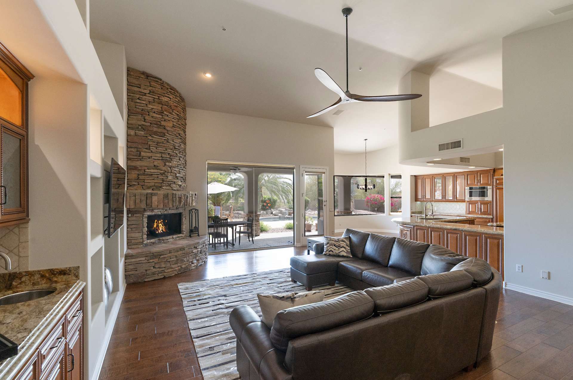 8 of 65. Designed for connection and comfort, this great room features vaulted ceilings, a curved stone fireplace, and fluid access to the kitchen and backyard ideal for both daily living and entertaining guests.