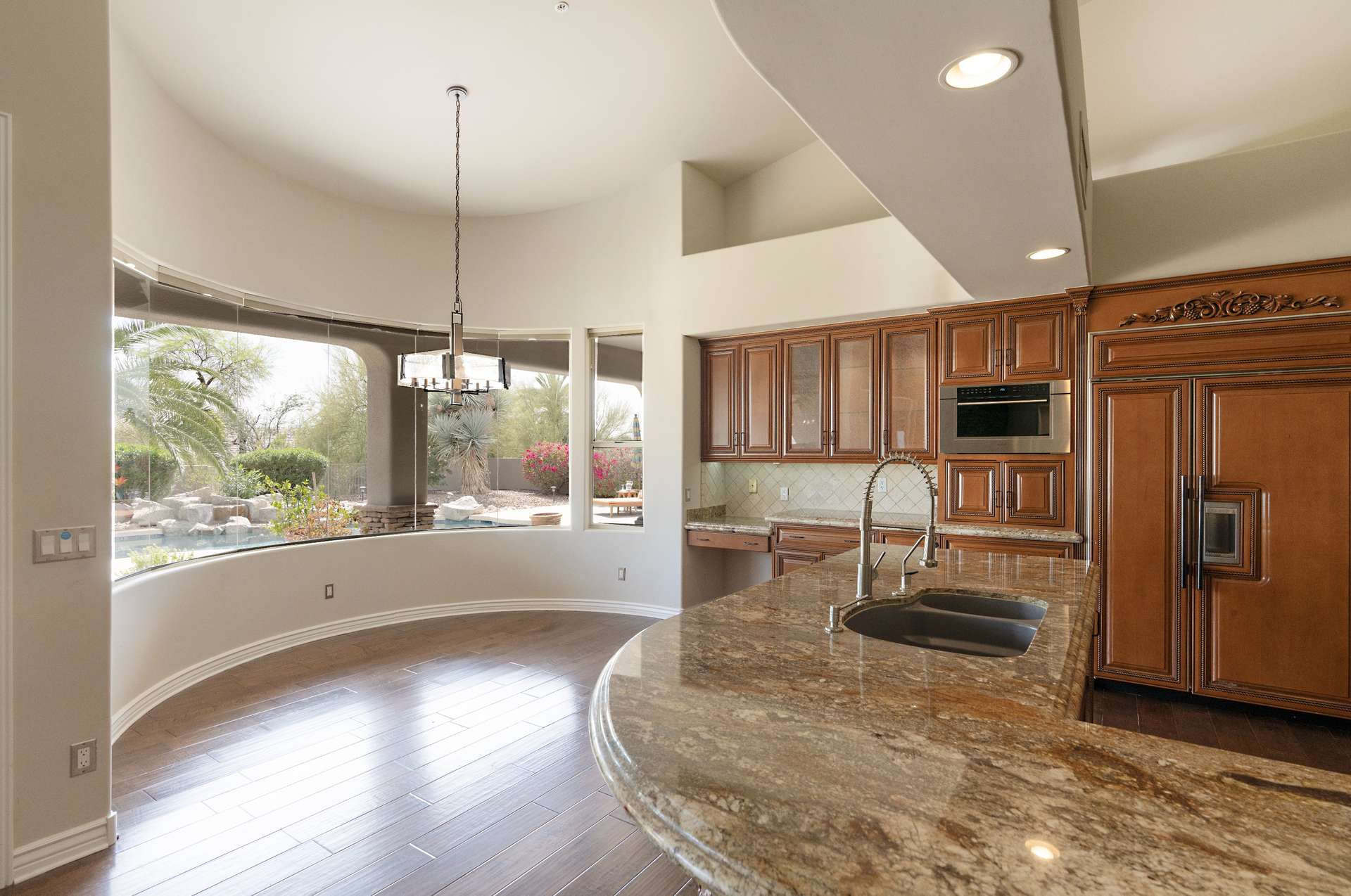 10 of 65. Bask in morning light in this rounded breakfast nook with panoramic backyard views. Overlooking the pool and palm trees, this space brings natural serenity to every casual meal.
