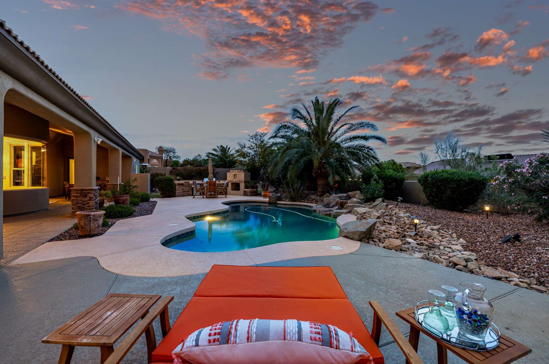 41 of 65. This evening view of the backyard oasis highlights a beautifully lit pool surrounded by desert palms and manicured landscaping. From peaceful lounging to vibrant gatherings, this Scottsdale space was designed for refined outdoor living.