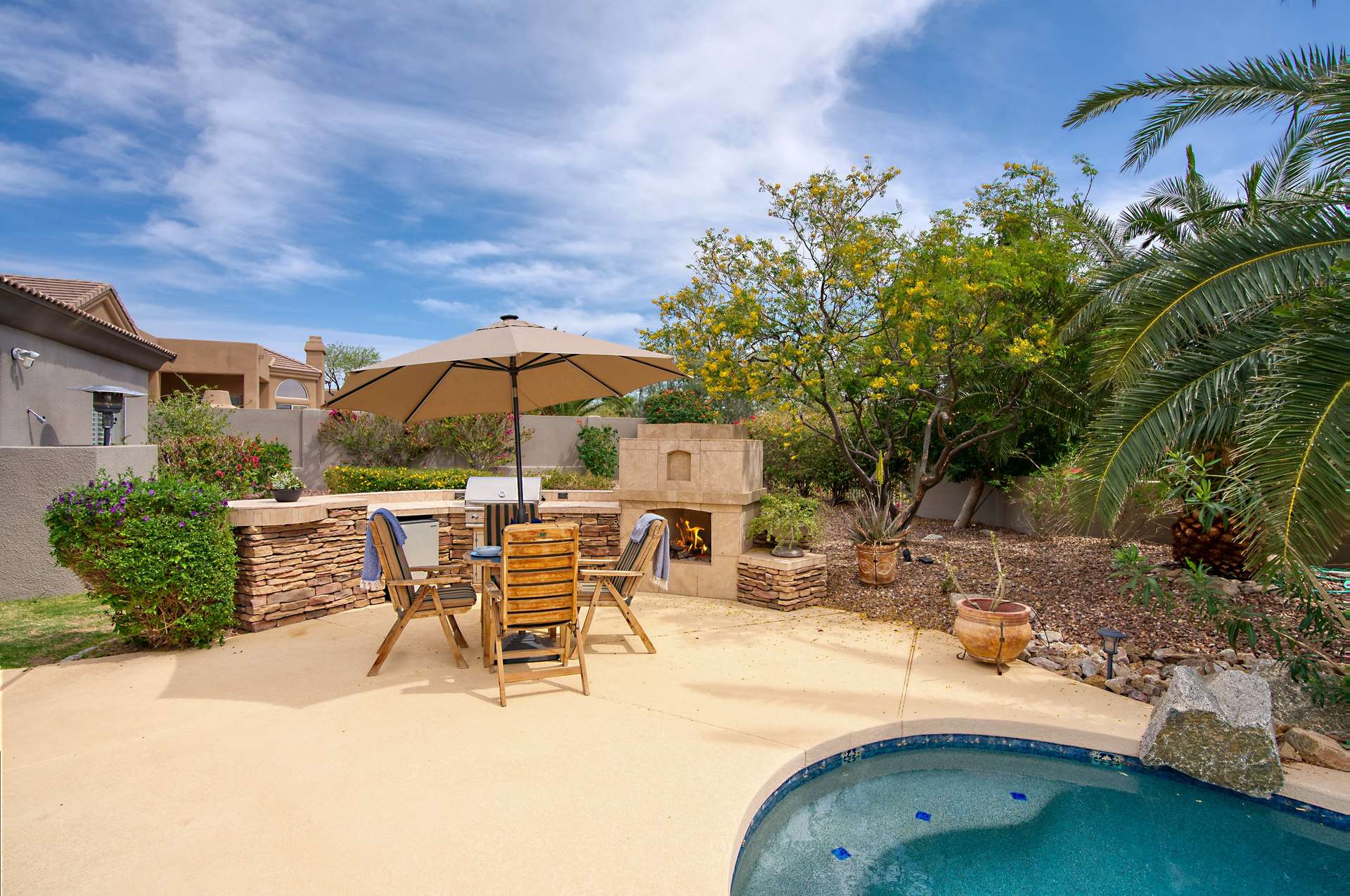 46 of 65. A shaded dining area by the pool offers versatility for entertaining, from casual barbecues to evening cocktails. The built-in grill and fireplace make this space a fully functional outdoor extension of the home.