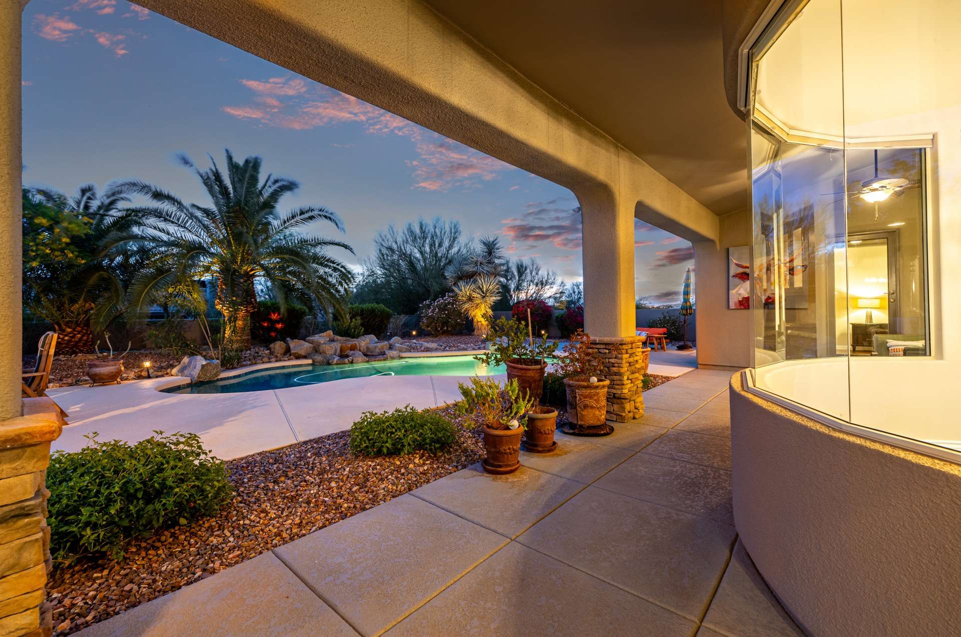 51 of 65. Step outside to a beautifully shaded patio overlooking the pool and vibrant desert landscaping. Framed by architectural columns and blooming flora, this covered space invites relaxed mornings and peaceful evenings in Arizona s mild climate.