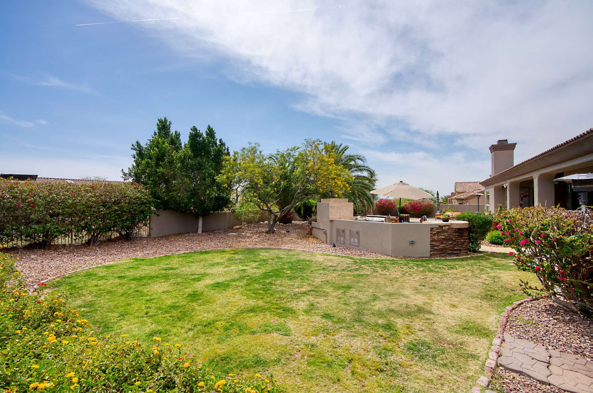 53 of 65. Enjoy outdoor gatherings in this generous backyard space featuring a grassy lawn and built-in BBQ station. With mature landscaping and stone-accented finishes, the area is ideal for entertaining or playing under the Arizona sun.